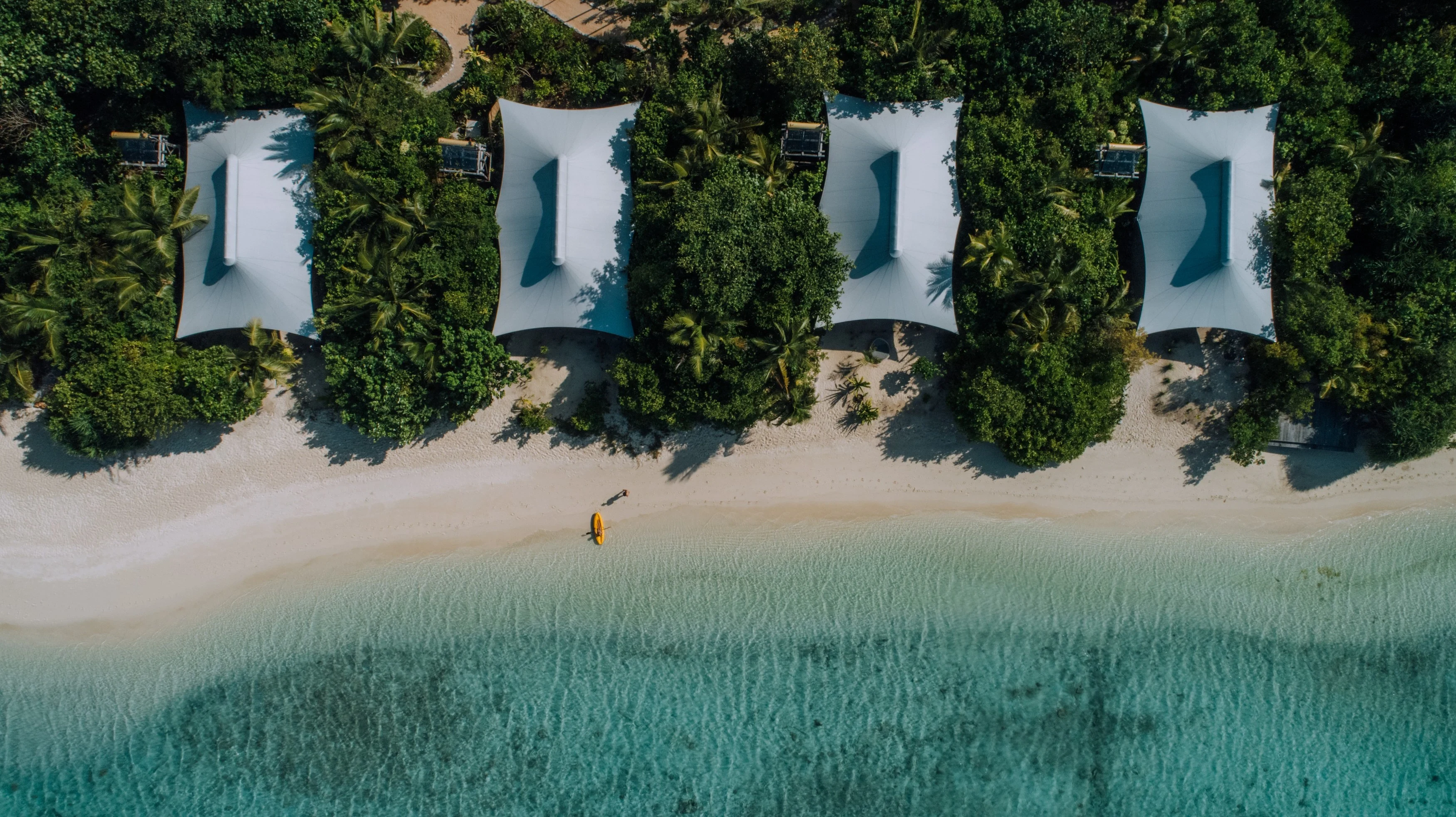 aerial_man_walking_to_yellow_kayak_in_front_of_beach_suites.webp